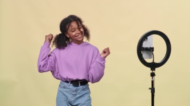 かなり暗い皮をむいた少女は ソーシャルネットワークのためのスマートフォンでビデオを撮影しながら ベージュの背景で音楽に踊ります — ストック動画