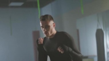 Dövüşçü boks salonunda yumruklarını ve savunmasını eğitir. Boksör antrenman yapar ve kameraya bakar..