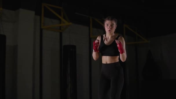 女子拳击手训练他的腿 在拳击馆训练 年轻女子看着摄像机 训练了一系列拳打脚踢 4K慢动作 — 图库视频影像