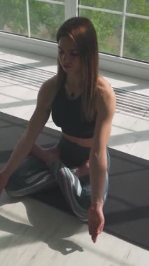Sağlık, genç bir kadın meditasyon yapıyor ve yoga yapıyor, sakin bir ruh hali, ışıkla dolu beyaz bir odada dinleniyor, kız yerde oturuyor, sosyal ağlar için dikey bir video..