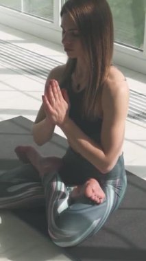 Sağlık, sportif kadın meditasyon yapıyor ve yoga yapıyor, sakin bir ruh hali, ışıkla dolu beyaz bir odada dinleniyor, kız yerde oturuyor, sosyal ağlar için dikey bir video..