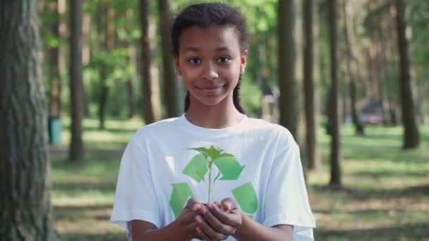 自然を大切にする 若いダークスキンガールのボランティアは 彼女の手に小さな花の植物を保持し カメラを見て 比喩的な行動 自然は私たちの手にあります — ストック動画
