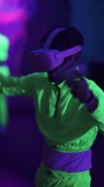 Etkileşimli teknolojiler, sanal gerçeklik gözlüklü bir adam atari oyunu oynar, neon eğlence parkında oyuncu, mor ışık, dikey video oyunu.