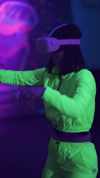 垂直ビデオ バーチャルリアリティグラスの女性は アーケードゲームを果たしています ネオンアミューズメントパークでプレーヤー 紫色光 — ストック動画