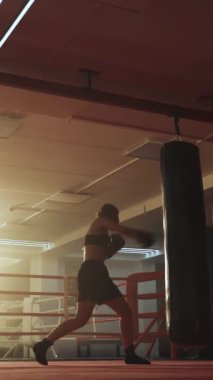 Kadın boksör yumruklarını eğitiyor, kum torbasını dövüyor, boks salonunda antrenman günü, dikey video..