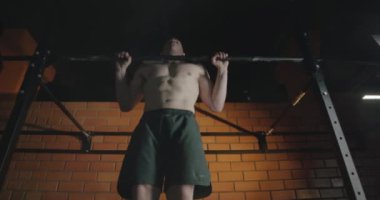 Spor salonundaki atletik adam, yatay demirde barfiks çekiyor..