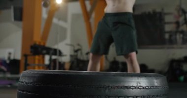 Kaslı bir adam balyozla lastiğe vurur, çekiçle kavis yapar..