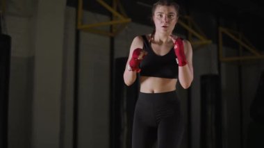 Kadın dövüşçü, boks salonunda antrenman yapıyor, genç kadın kameraya bakıyor ve bir dizi tekme eğitiyor..