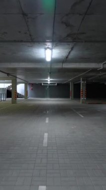 Yeraltı otoparkında yürümek, bir ofis binasının otoparkında düzgün kamera hareketi, dikey video, beton duvarlı boş alan.
