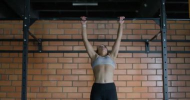 Genç bir kadın barfiks çekiyor. Yatay çubukta. Spor salonunda antrenman günü..