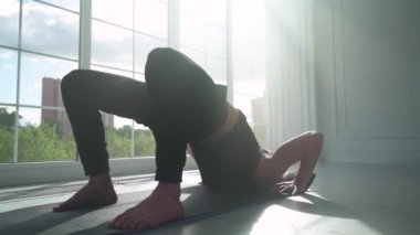 Sakinlik, ışıkla dolu beyaz bir odada yoga yapan genç bir adam, büyük pencerenin yanında kaslarını esnetiyor..