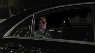 Hareketli bir arabada odaklanmış bir iş adamı, takım elbiseli üst düzey bir yönetici bir iş arabasının arkasında oturuyor, gece yolculuğu, 4K yavaş çekim.