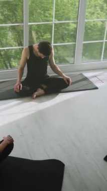 Genç adam meditasyon yapıyor ve yoga yapıyor, sakin bir ruh hali, ışıkla dolu beyaz bir odada dinleniyor, adam yerde oturuyor, sosyal ağlar için dikey video..