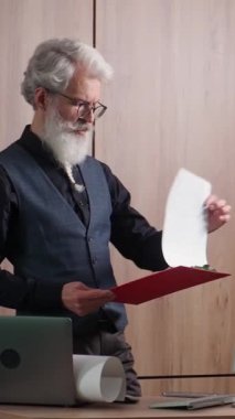 El bilgisayarı, gri saçlı mimar nesnelerin çizimlerini kontrol eder, düşünceli üniversite öğretim görevlisi belgeleri kontrol eder, tasarımcı iş yerinde, dikey video.