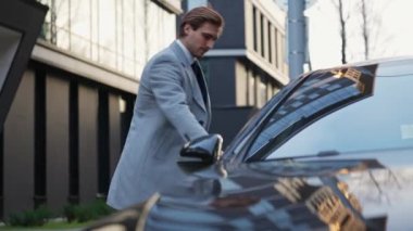 Genç işadamı siyah bir arabaya doğru yürür ve yolcu koltuğuna oturur. Takım elbiseli zarif bir adam toplantı için ayrılır. Arka plandaki ofis binası..