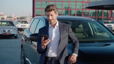 Takım elbiseli genç bir işadamı yeni arabanın yanında duruyor ve akıllı telefon kullanıyor, neşeli bir adam yeni bir arabaya biniyor, kiralık bir arabayla geziye çıkıyor..
