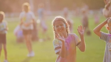 Varşova, Polonya - 18 Ağustos 2024: Holi festivali, yaz zamanı, neşeli çocuklar birbirlerine renkli toz fırlatıyor, arka planda kutlama yapan kalabalık, mutlu çocukluk.