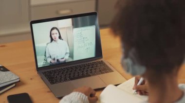 Giyinik, esmer tenli bir kız bir masada oturur ve bir dizüstü bilgisayar kullanarak internetten ders çalışır, uzaktan öğrendiği bir videoda öğretmeniyle, uzaktan eğitimle, geçmişine bakarak öğrenir..