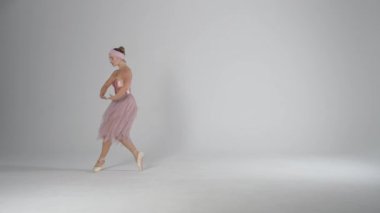 Pembe etekli zarif balerin beyaz arka planda dramatik danslar ve koreografik öğeler sergiledi, rüzgarlı ve güzel bir dans, yavaş çekim..