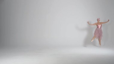 Pembe etekli güzel balerin beyaz arka planda dramatik danslar ve koreografik elementler sergiliyor, rüzgarlı ve güzel bir dans, yavaş çekim..