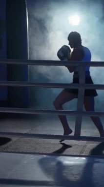 Sportif kadın kum torbasını yener, boks salonunda antrenman günü, boksör onun tekmelerini ve yumruklarını eğitir, güçlü vücut, dikey video, bulanık görüş..