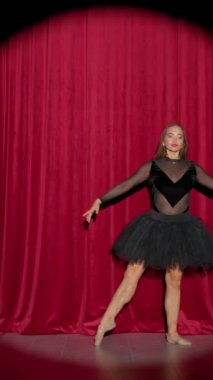 Dramatik bir performans, siyah etekli güzel bir balerin kırmızı arka plan, sahne ışığı, dikey video üzerinde dramatik dans ediyor..