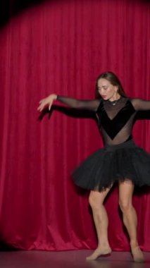 Dikey video, dramatik performans, siyah etekli güzel balerin kırmızı arka planda, sahne ışığı altında dramatik dans gösterisi..