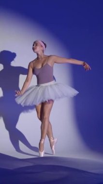 Beyaz etekli balerin mavi arka planda dramatik elementler sergiler, rüzgarlı ve güzel dans, mavi ışık ve hava kumaşı arka planda, yavaş dikey video.