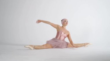 Performans, pembe etekli zarif balerin beyaz bir arka plandaki performansa hazırlanmak için kaslarını ısıtır ve gerer..
