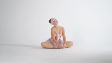 Pembe etekli balerin ısınıyor ve kaslarını esnetiyor. Beyaz arka planda, yavaş çekimde bir performansa hazırlanıyor..
