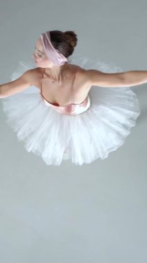 Dikey video, pembe etekli balerin dansı ve beyaz arka planda dramatik koreografikler sergilemek..