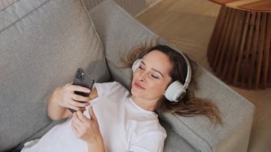 El bilgisayarı, neşeli bir kadın kanepede uzanıyor ve akıllı bir telefonla selfie çekiyor, kulaklıkla müzik dinliyor, kamera titriyor..