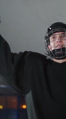 Profesyonel bir hokey oyuncusunun portresi, maçtaki zafere seviniyor, siyah üniformalı bir adam kollarını sallıyor, dikey video, bulanık görüş..