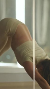 Gergin, dikey video, aynalı odada yoga yapan kadın, esnek kadın yoga öğeleriyle esneme hareketleri yapıyor..