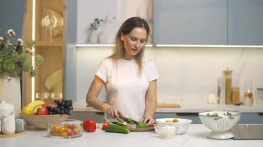 Ev mutfağında sabah, neşeli bir kadın sebze salatası hazırlıyor, avokadoyu küçük parçalara ayırıyor, sağlıklı yemekler yiyor..
