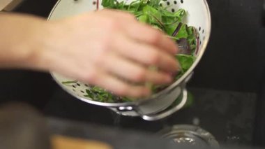 Yavaş çekim, ellerin yakın görüntüsü, kadın salata için taze ıspanak ve yeşillikleri yıkıyor, sağlıklı bir yemek hazırlıyor..