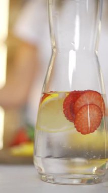 Dikey video, kadın ferahlatıcı çilekli limonata yapıyor, sabah mutfakta, su dengesi....