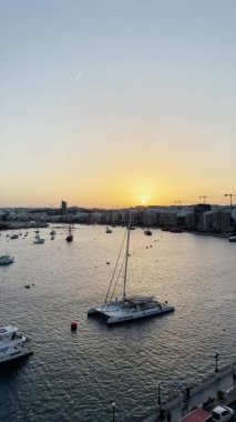 Malta, Valletta - 22 Mart 2025: Güney Avrupa, güzel günbatımı manzaralı yatlar ve eski kasaba, mimarlık ve yat limanı, Malta, Valletta durağan arka plan.