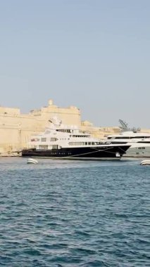 Malta, Valletta - 23 Mart 2025: Eski kasabanın yakınlarındaki büyük yatların güzel manzarası, mimari ve yat limanı, dikey video manzarası, körfez manzarası, Valletta.