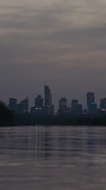 Varşova, Polonya - 17 Nisan 2025: Akşam manzarası, ufuktaki gökdelenlerin dikey videosu, şehir nehri ve şehir merkezi manzarası, bir gece iş merkezi.