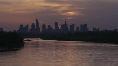 Bulanık manzara, akşam manzarası, gökdelenler ufukta siluetler, nehir ve gün batımı gökyüzü manzarası, hızlı hareket, gece vakti iş merkezi.