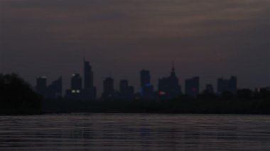 Bulanık arka plan, akşam şehir manzarası ufukta gökdelenler, nehir ve günbatımı gökyüzü, gece vakti iş merkezi..