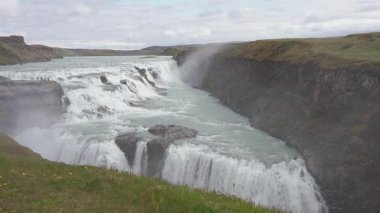 Devasa şelale manzarası, İzlanda doğa manzarası, şelalenin dinginlik manzarası, eriyen buzul su akışı, turistik yerler ve yollar, yeşil kayalık arazi.