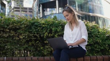 Odaklanmış bir kadının portresi, beyaz gömlek giyen, laptopta çalışan, dışarıda bilgisayar okuyan, olgun bir öğrenci, rüzgarlı bir hava..