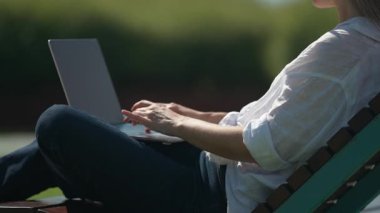 Yavaş çekim, dizüstü bilgisayarda çalışan odaklanmış bir kadın, dışarıda laptopla çalışıyor, olgun bir öğrenci daktilo metni kullanıyor, güneşli bir hava var..