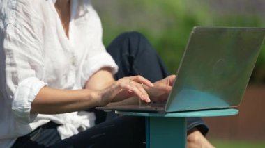 El bilgisayarı, beyaz tişört giyen, laptopla çalışan, dışarıda ders çalışan, yetişkin öğrenci daktilo metni kullanan, rüzgarlı hava koşulları olan bir kadın..