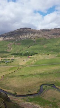 İzlanda manzarası, ihtişamlı doğa geçmişi, dağ vadisine karşı turistik yerler ve evler, yükseklikten, turistik altyapıdan, toprak dokusundan, doğa arka planından volkanik bir vadi manzarası.