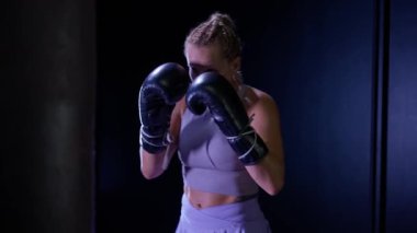Ağır çekimde, profesyonel boksör yumruklarını eğitiyor, karanlık boks salonunda antrenman yapıyor, kadın boksör bir dizi yumruk ve portre eğitiyor..