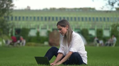 Ağır çekimde, yeşil alanda oturan ve laptopla çalışan güzel bir kadın. Şehir parkında dizüstü bilgisayar kullanan, yetişkin bir öğrenci daktilo metni yazan biri..