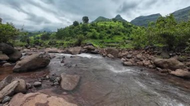 Ormandaki kayaların üzerinden akan sakin bir akarsu manzarası, doğanın rahatlatıcı seslerini ve canlı yaprakları sergiliyor.